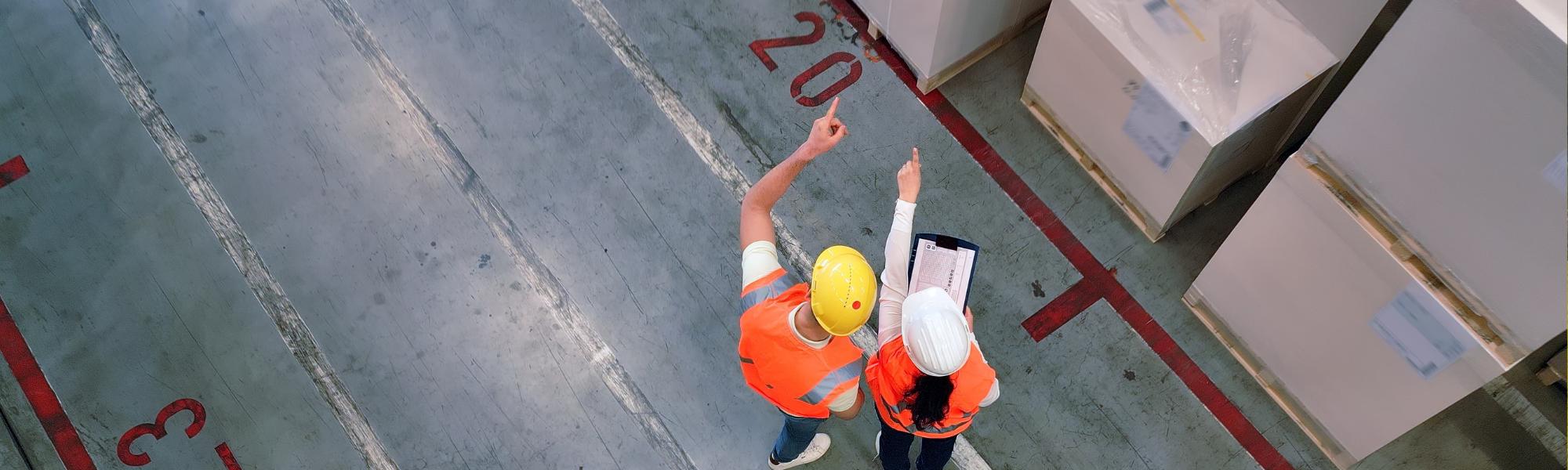 Two procurement professionals in hard hats looking and pointing at boxes