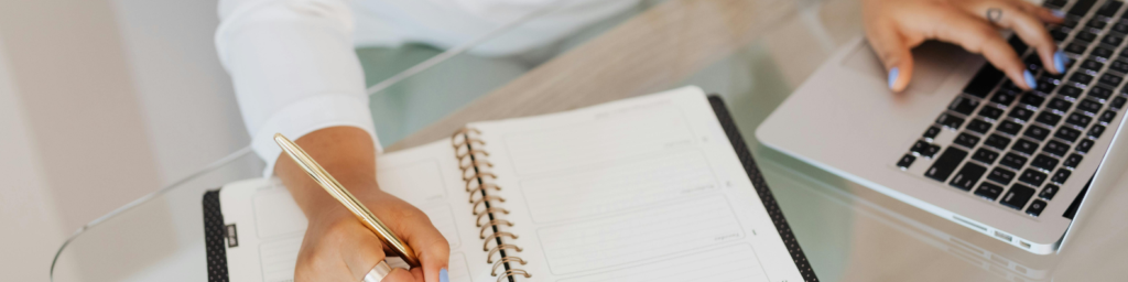 Hands of an executively dressed person using notepad and laptop