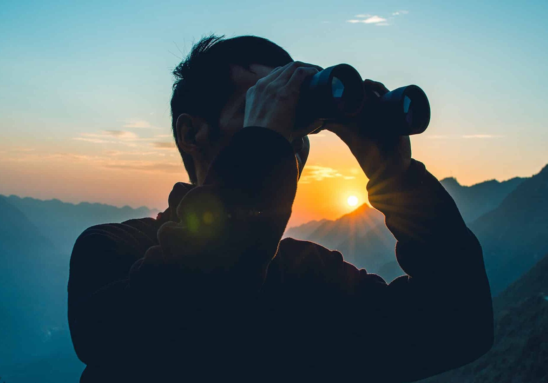 search & selection main image 2000x1300 Man searching in binoculars with sunset behind him